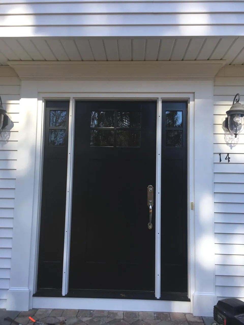 Black entry door with divided-light glass, matching sidelights, and polished nickel handleset on a white clapboard home
