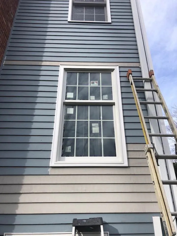 Tall double-hung replacement window with fresh white casing on blue clapboard siding