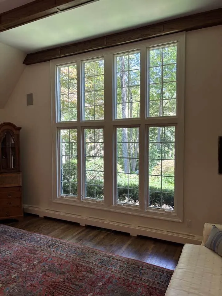 Wall of four tall grid-pattern windows overlooking woods, framed by exposed wood beams in a living room
